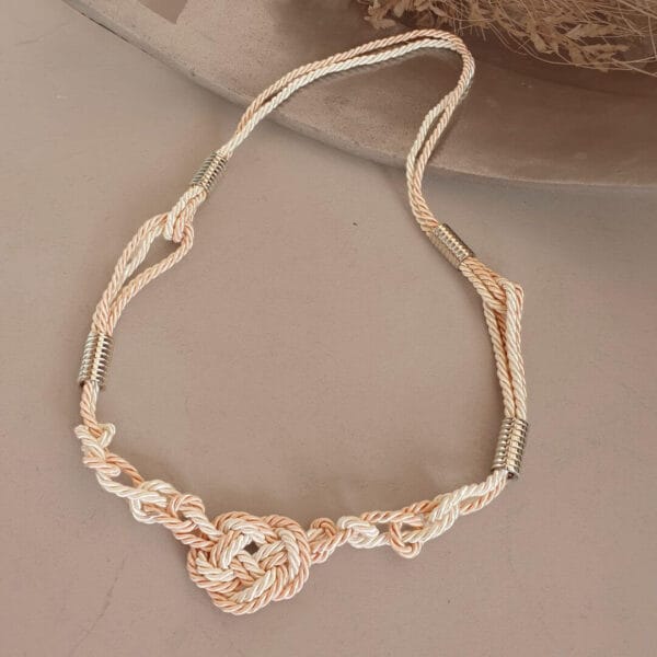 colar de macrame em corda de viscose e algodão, na combinação de cores rosa e cru com detalhes em metal prateado