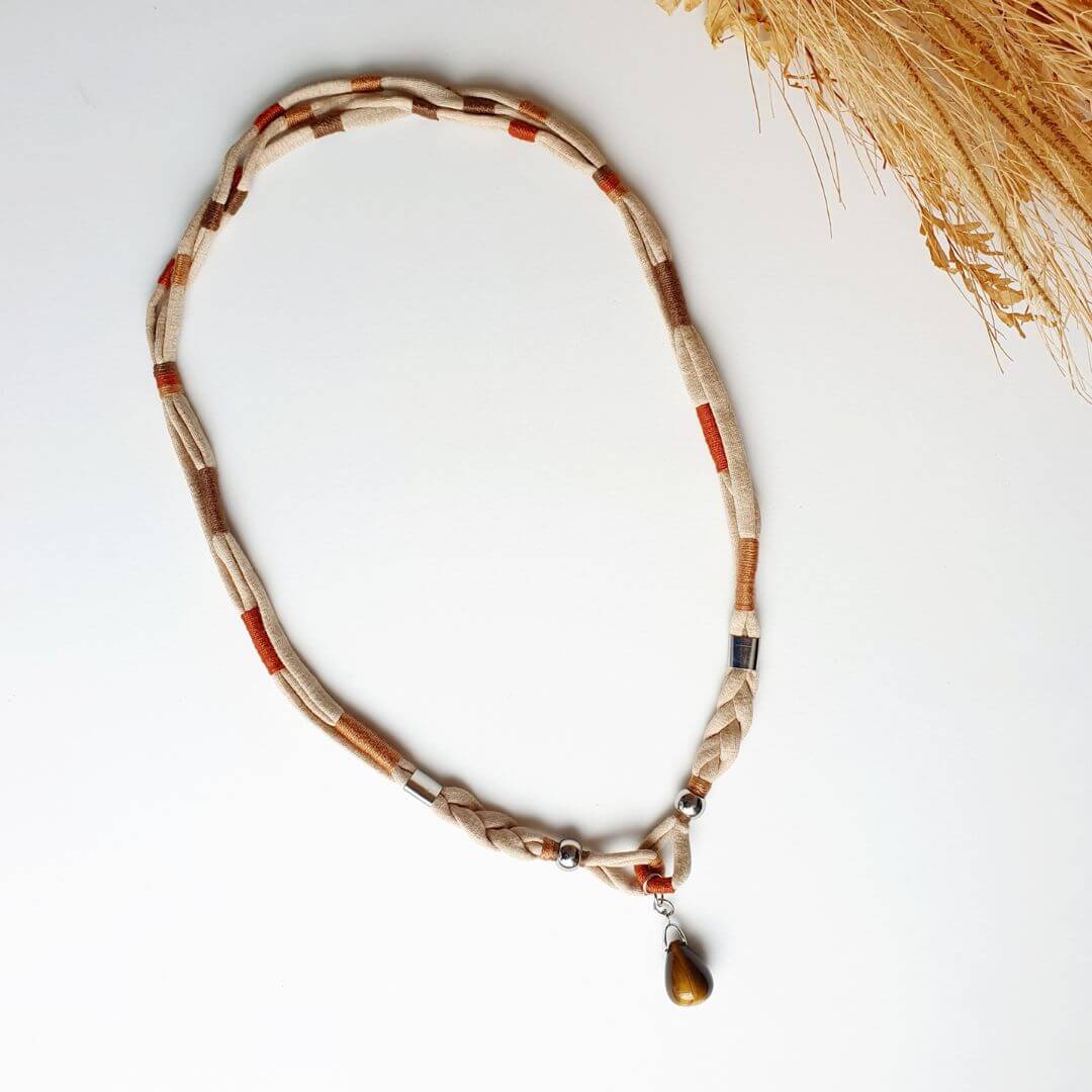 colar feito com fio de malha na cor bege e detalhes nas cores terracota, caramelo e marrom, com pendente de pedra Olho de tigre