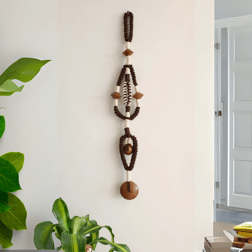 escultura têxtil de tamanho médio, feita com corda em duas cores e entremeios de madeira, pendurada na parede de sala com plantas ao redor